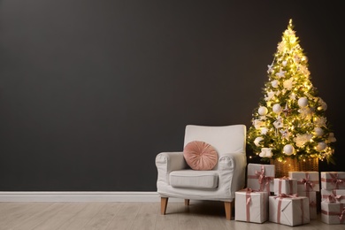 Photo of Beautifully decorated Christmas tree, gift boxes and armchair near black wall indoors, space for text