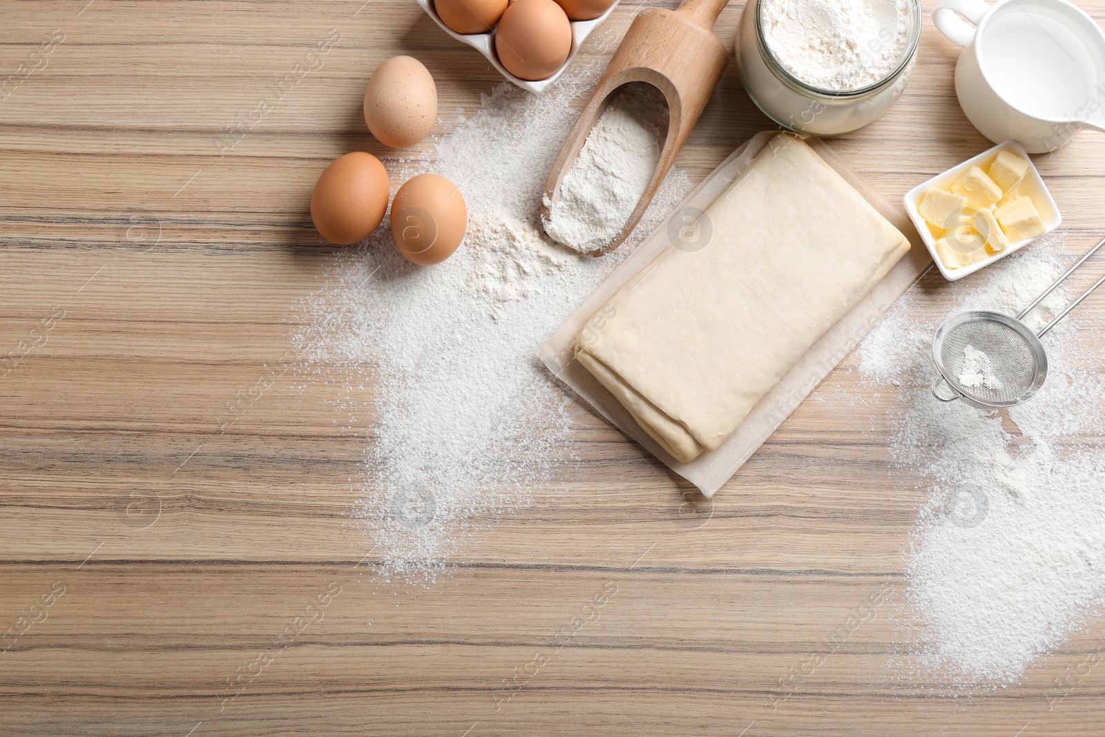 Photo of Puff pastry dough and ingredients on wooden table, flat lay. Space for text