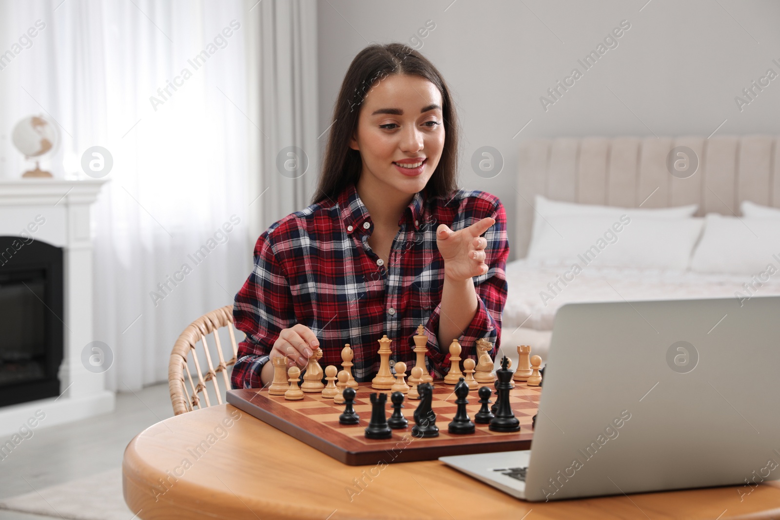 Photo of Young woman playing chess with partner through online video chat at home