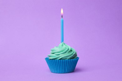 Delicious birthday cupcake with turquoise cream and burning candle on violet background