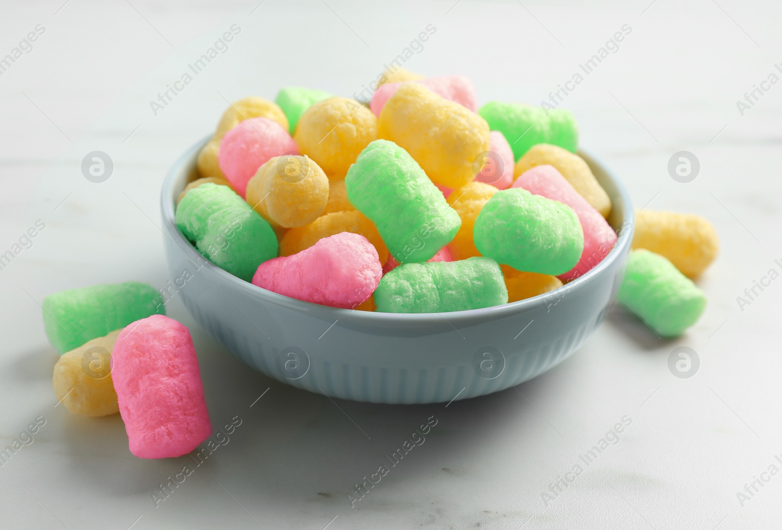 Image of Bowl with colorful corn puffs on white marble table, closeup