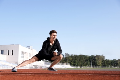 Young sportsman with wireless earphones stretching at stadium