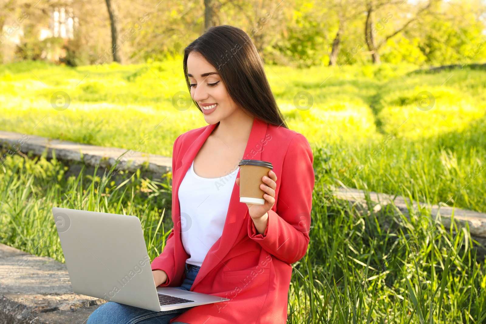 Image of Young woman with coffee using laptop outdoors