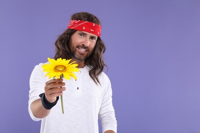 Photo of Stylish hippie man with sunflower on violet background, space for text