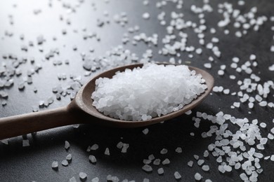 Photo of Natural salt and wooden spoon on black table, closeup