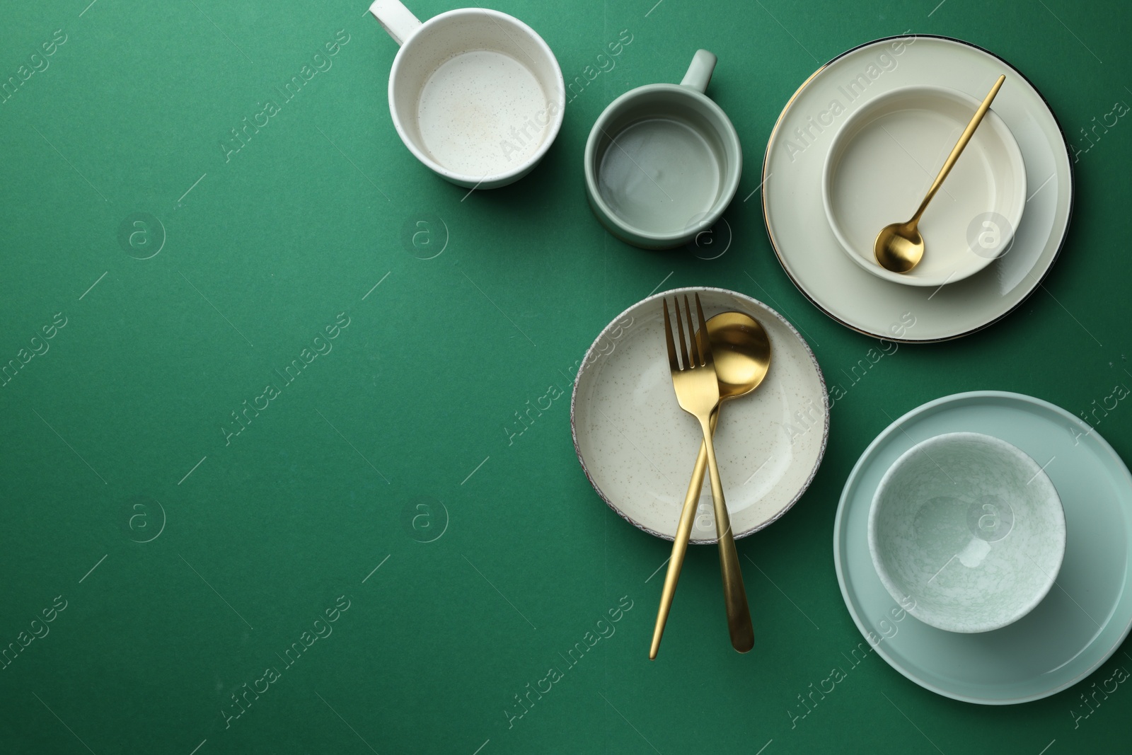 Photo of Stylish empty dishware and golden cutlery on green background, flat lay. Space for text