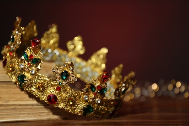 Photo of Beautiful golden crown and fairy lights on wooden table, closeup. Fantasy item