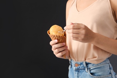 Photo of Woman eating yellow ice cream in wafer cone on black background, closeup. Space for text