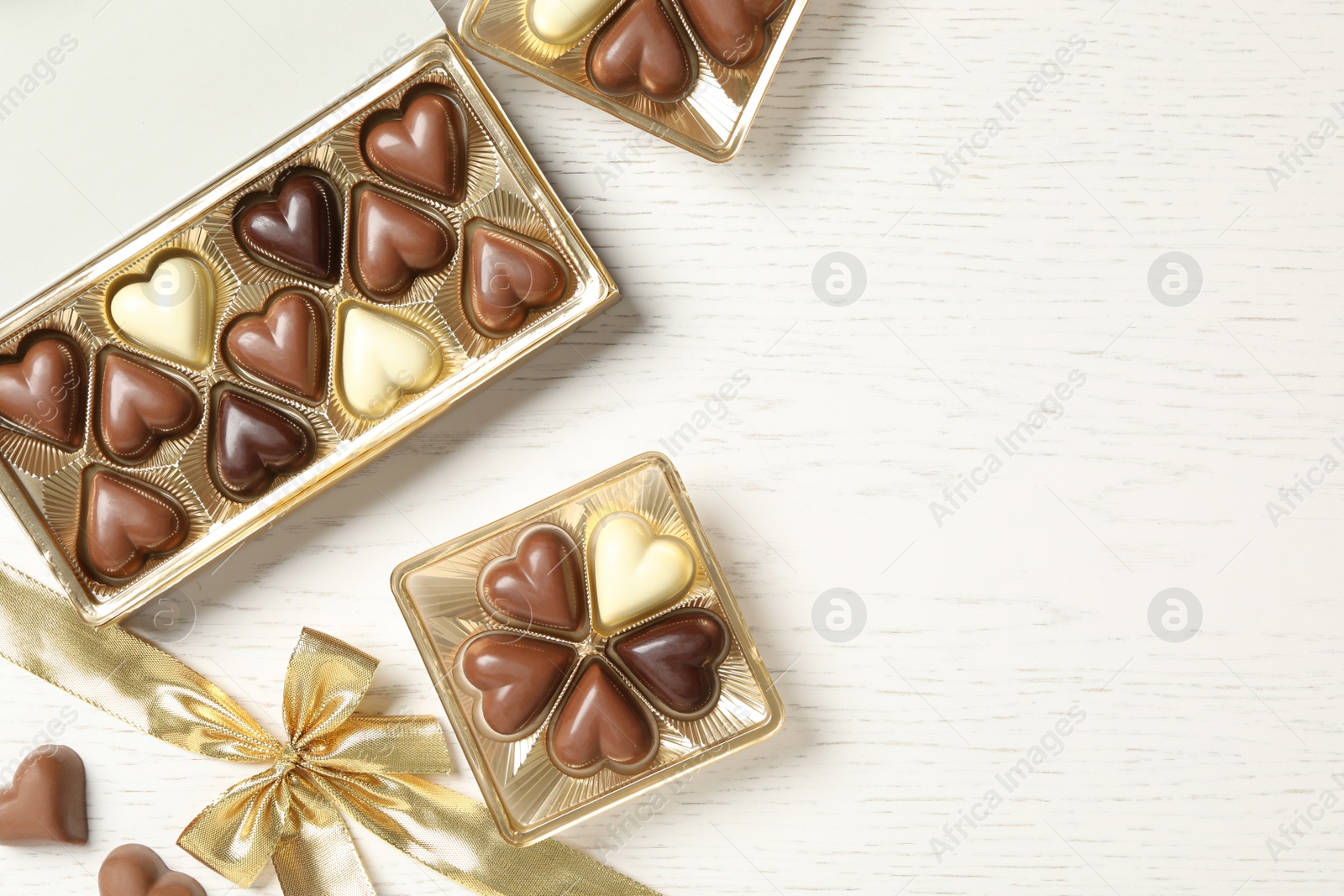 Photo of Beautiful heart shaped chocolate candies in boxes on white wooden table, flat lay with space for text