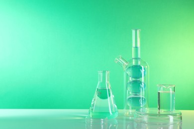 Laboratory analysis. Different glassware on table against green background, space for text