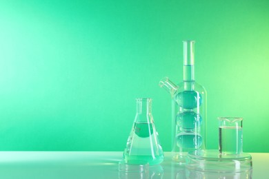 Photo of Laboratory analysis. Different glassware on table against green background, space for text