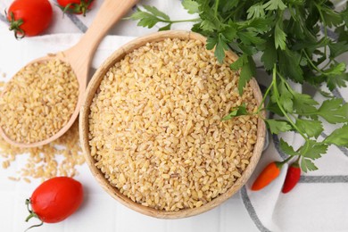 Photo of Raw bulgur in bowl, spoon, vegetables and parsley on table, flat lay