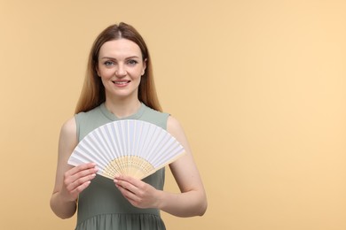 Happy woman with hand fan on beige background, space for text