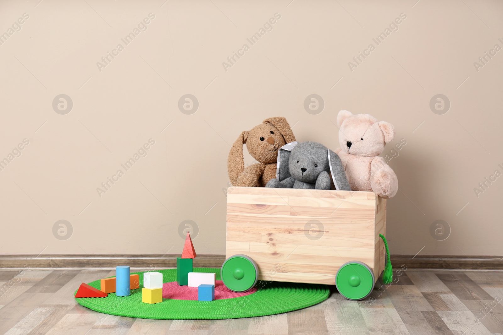 Photo of Wooden cart with stuffed toys and constructor on floor against light wall. Space for text