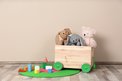 Wooden cart with stuffed toys and constructor on floor against light wall. Space for text