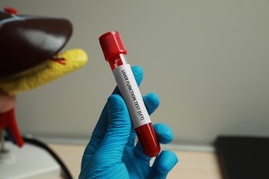 Photo of Laboratory worker holding tube with blood sample and label Liver Function Test on blurred background, closeup