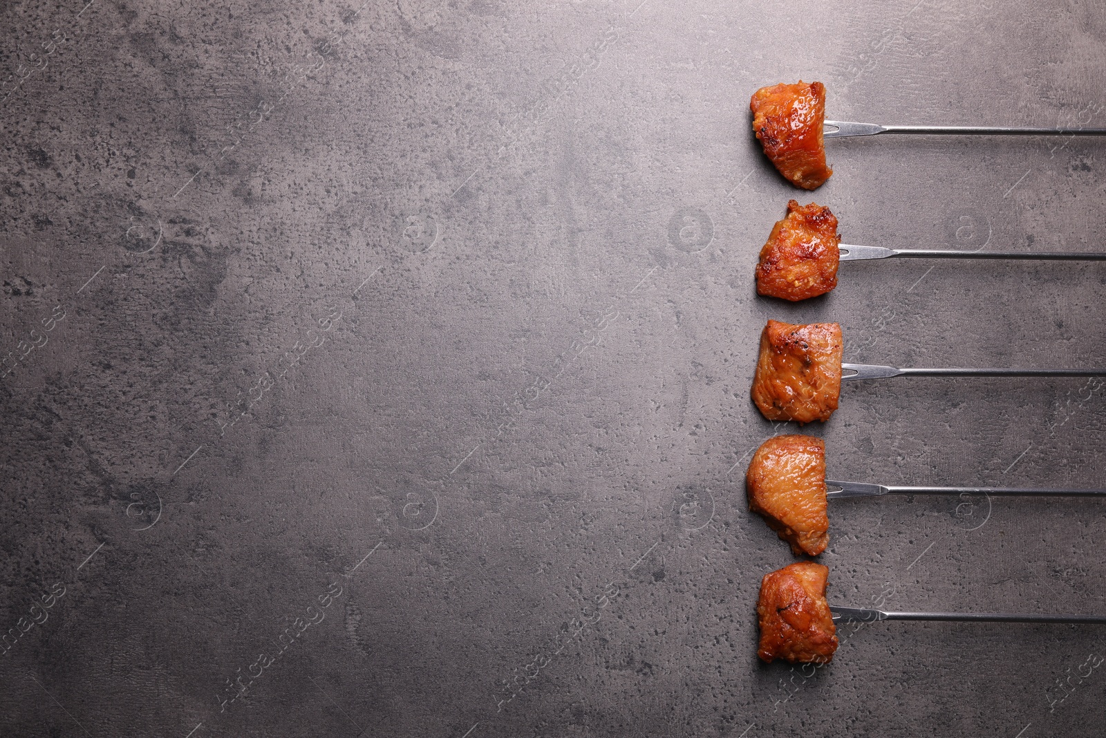 Photo of Fondue forks with pieces of fried meat on grey table, flat lay. Space for text