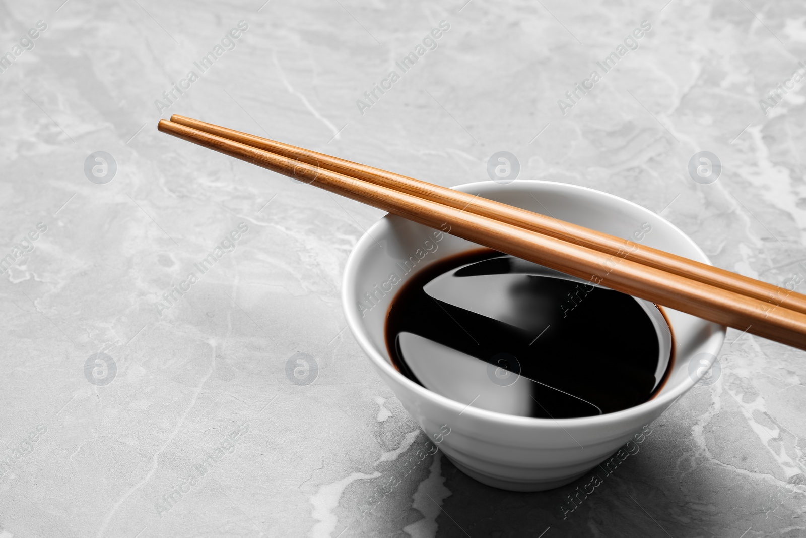 Photo of Bowl of soy sauce with chopsticks on marble background. Space for text