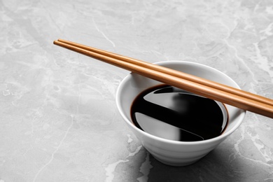 Photo of Bowl of soy sauce with chopsticks on marble background. Space for text