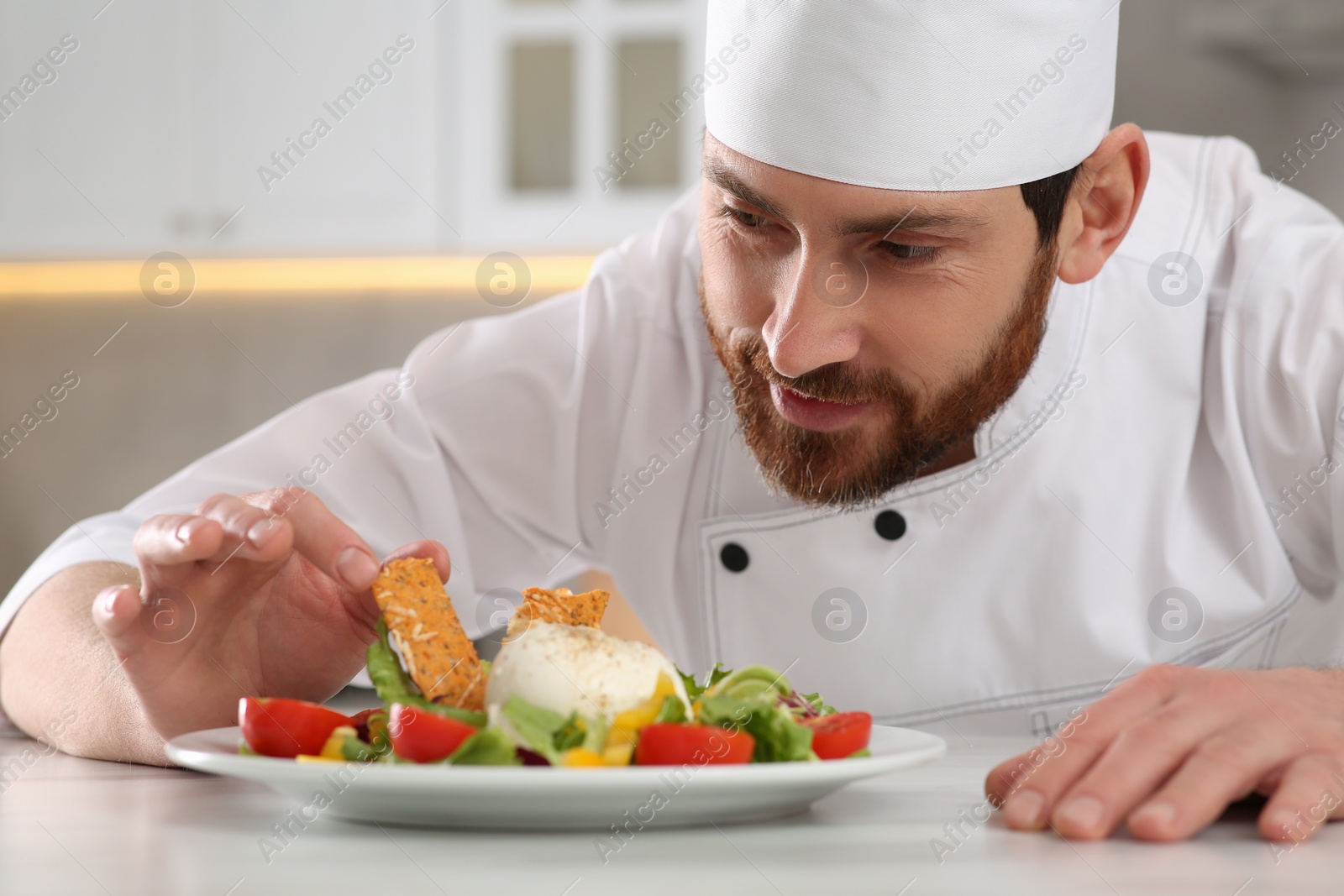 Photo of Professional chef decorating delicious salad with crispy bread at marble table in kitchen