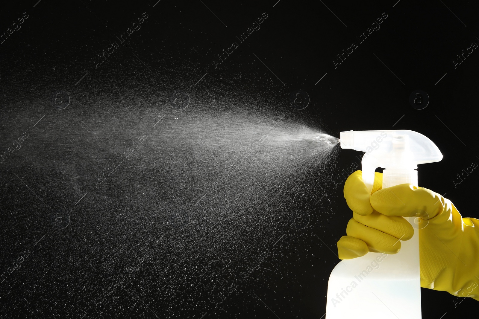 Photo of Woman spraying liquid from bottle on black background, closeup