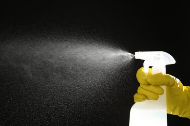 Photo of Woman spraying liquid from bottle on black background, closeup