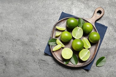 Fresh ripe limes and leaves on grey table, top view. Space for text