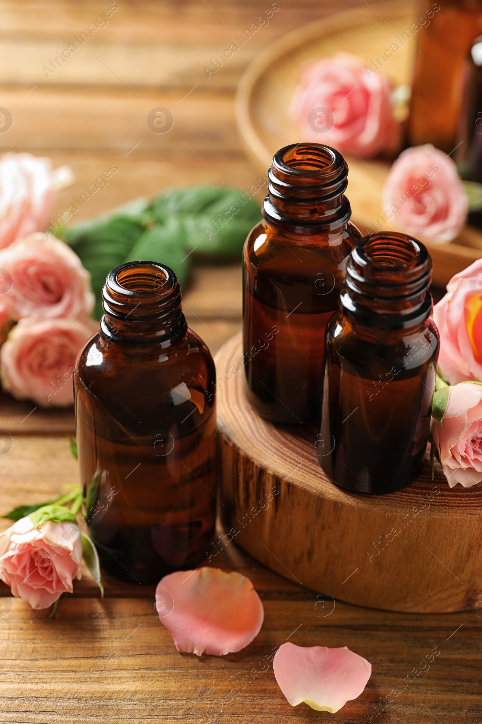 Photo of Bottles of rose essential oil and fresh flowers on wooden table