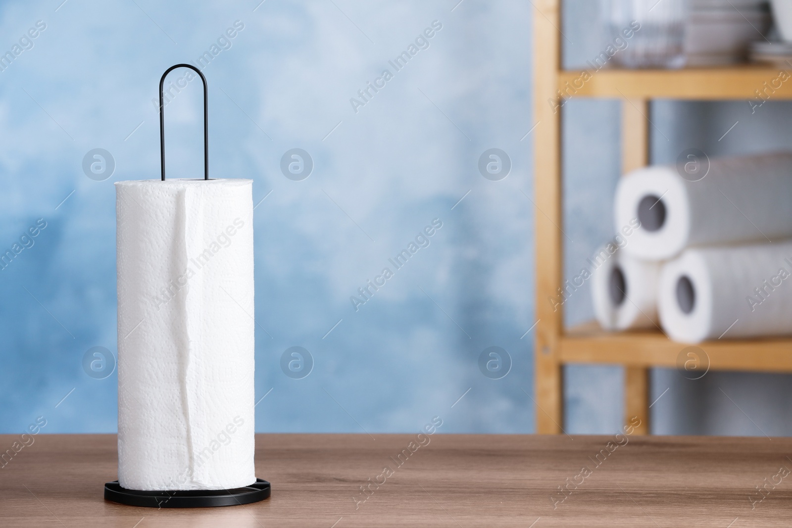 Photo of Holder with roll of white paper towels on wooden table indoors. Space for text