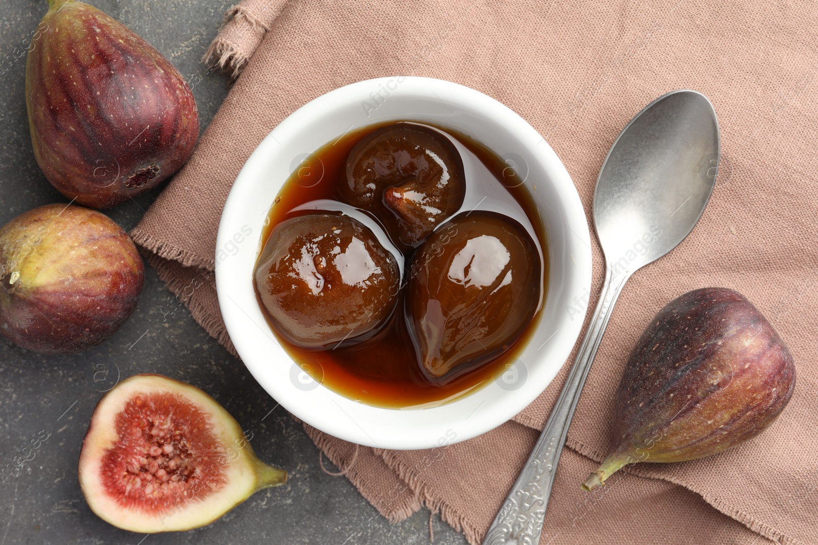 Photo of Bowl of tasty sweet jam, fresh figs and spoon on grey table, flat lay