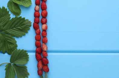 Photo of Grass stems with wild strawberries and leaves on light blue wooden table, flat lay. Space for text