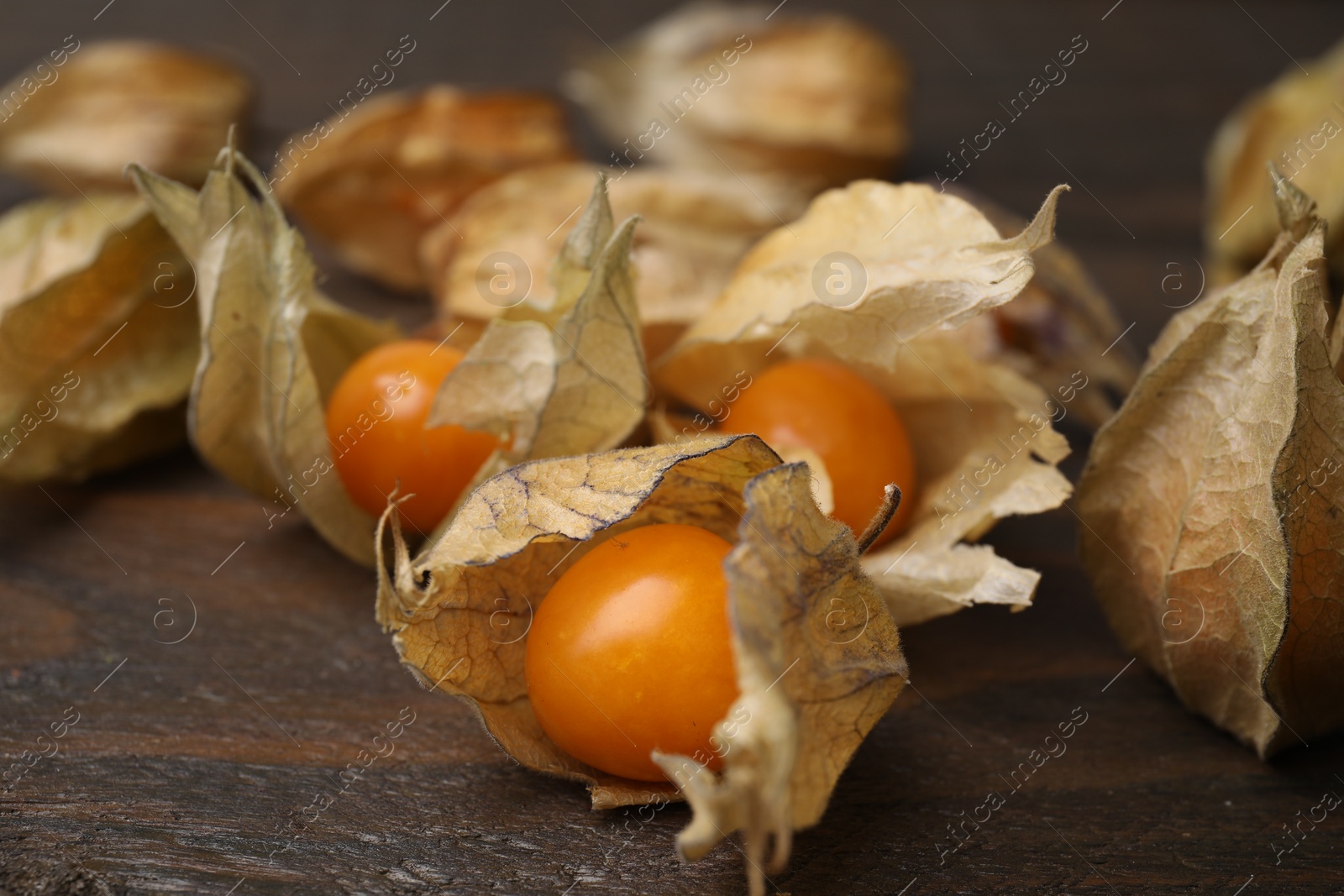 Photo of Ripe physalis fruits with calyxes on wooden table, closeup