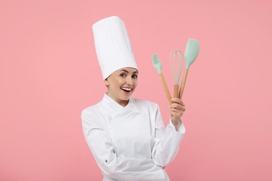 Photo of Happy confectioner in uniform holding professional tools on pink background