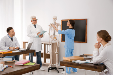 Medical students and professor studying human skeleton anatomy in classroom