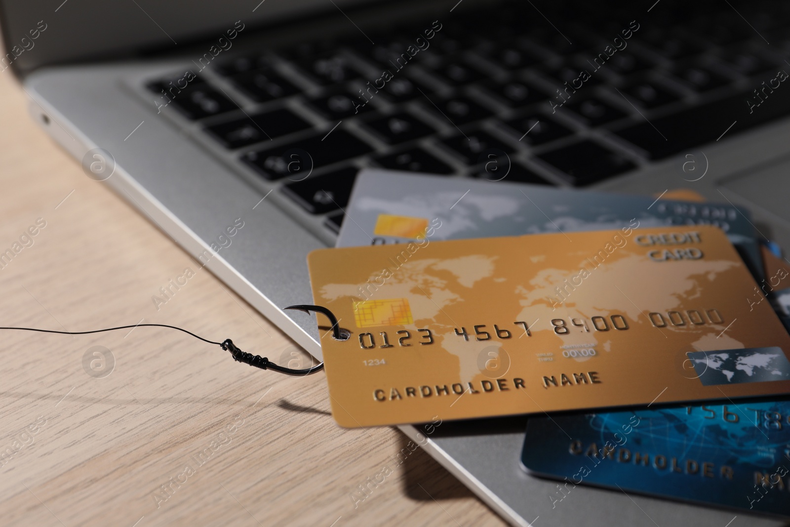 Photo of Fishing hook with credit cards and laptop on wooden table, closeup. Cyber crime