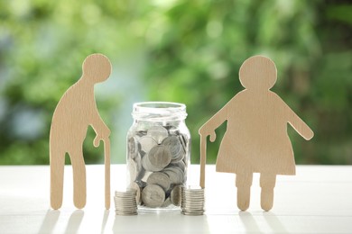 Photo of Pension savings. Figures of senior people and jar with coins on white table against blurred green background