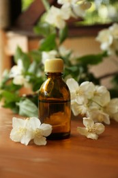 Bottle of jasmine essential oil and beautiful flowers on wooden table
