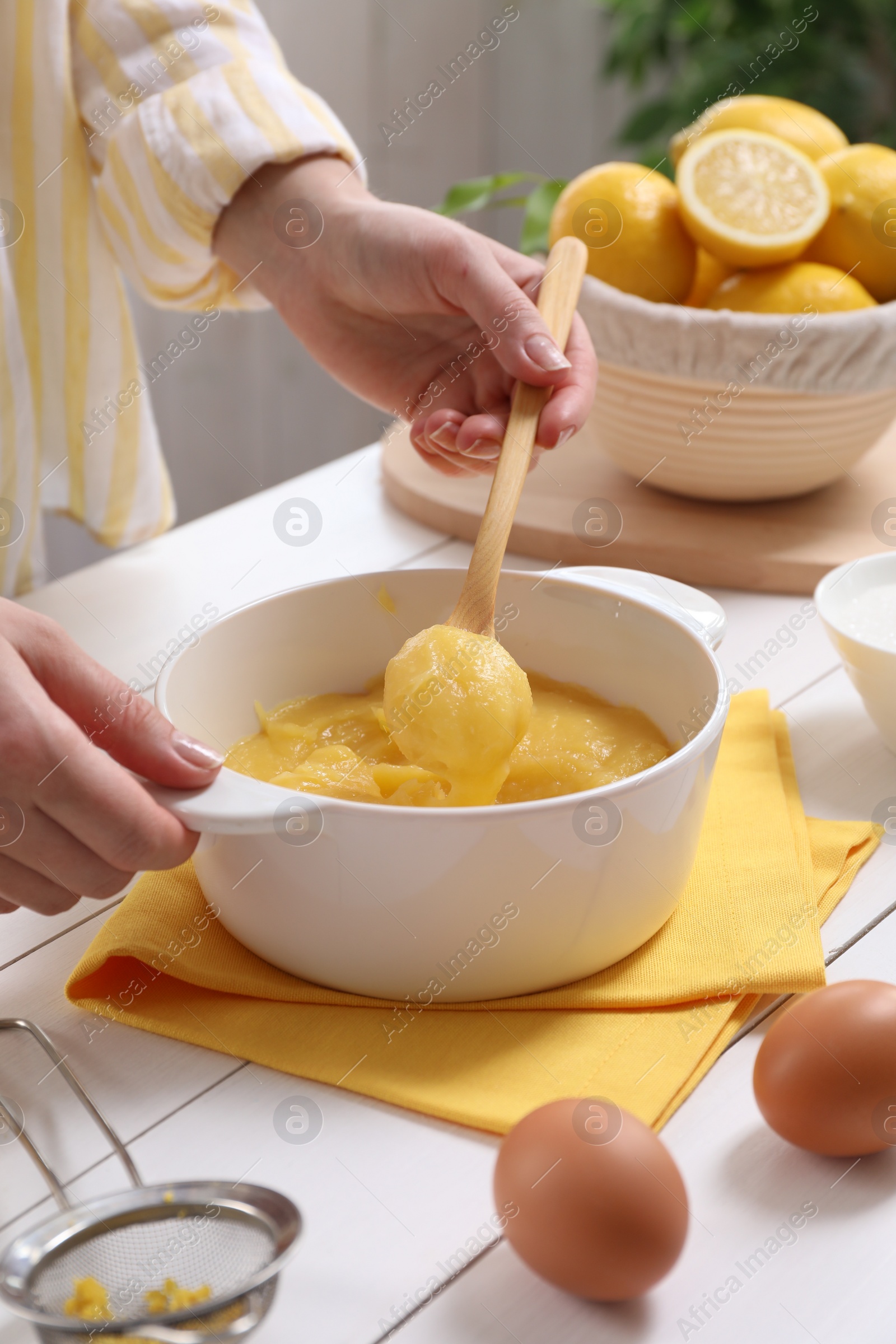 Photo of Woman cooking lemon curd at white wooden table, closeup