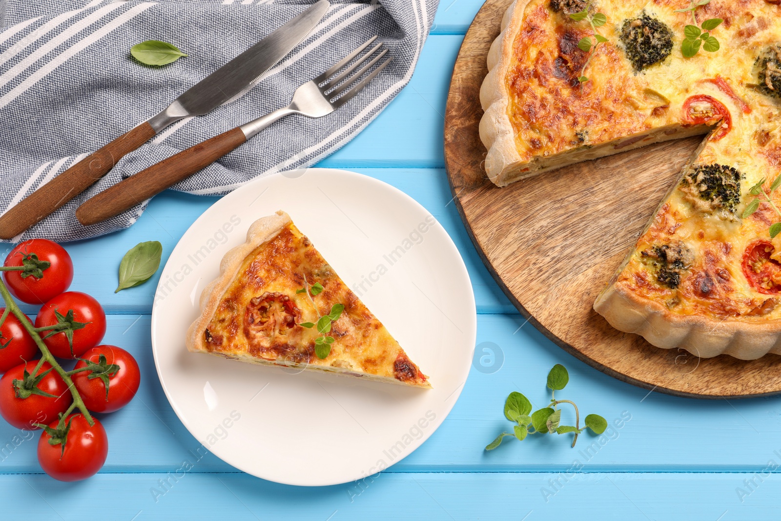 Photo of Delicious homemade vegetable quiche, tomatoes and cutlery on light blue wooden table, flat lay
