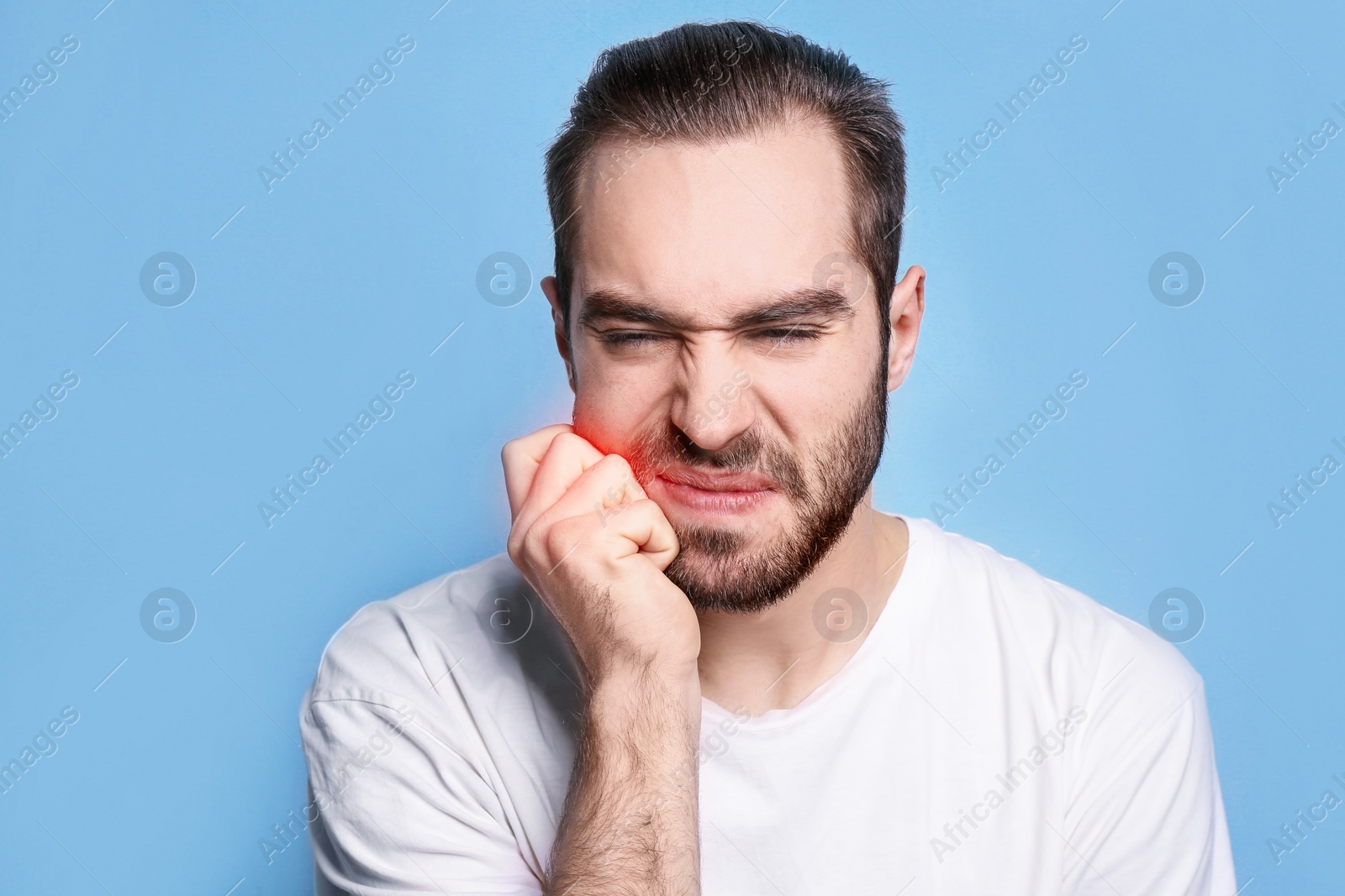 Image of Young man suffering from toothache on light blue background