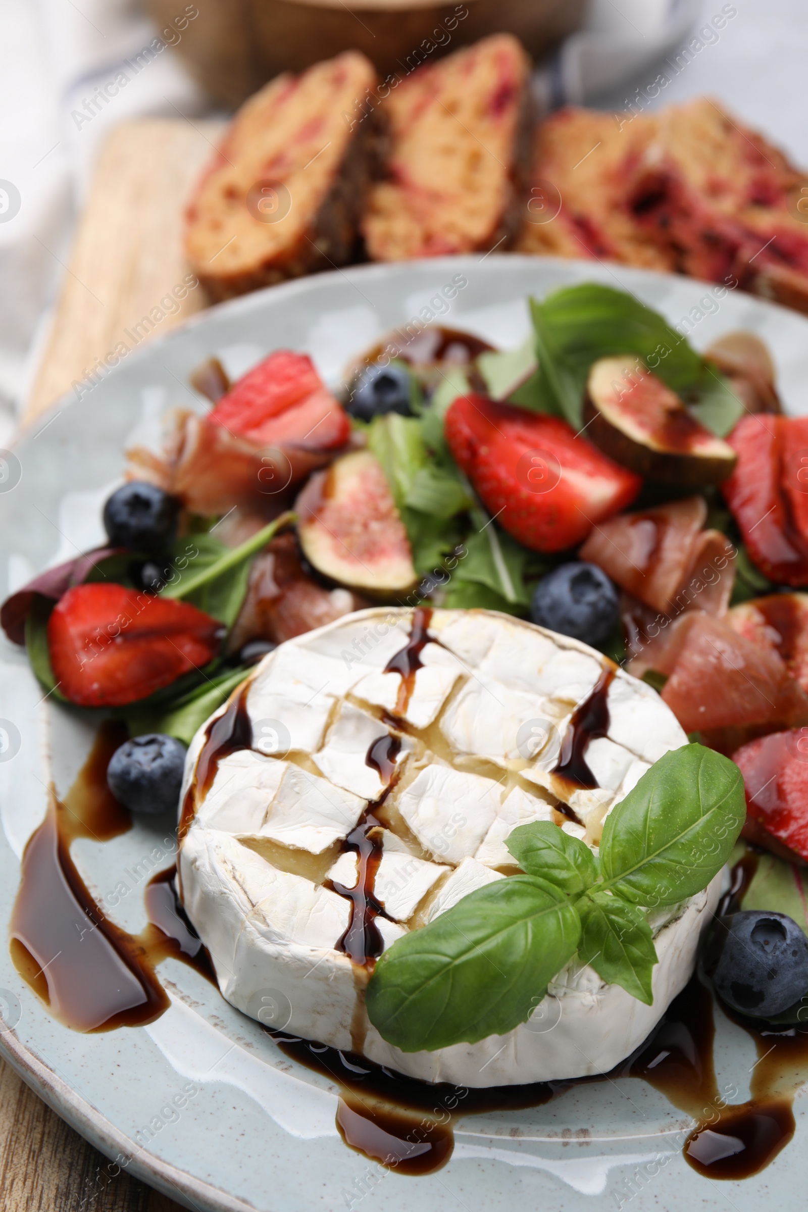 Photo of Delicious salad with brie cheese, berries and balsamic vinegar on table, closeup