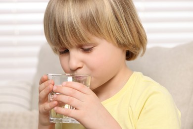 Photo of Cute little boy drinking fresh water from glass indoors