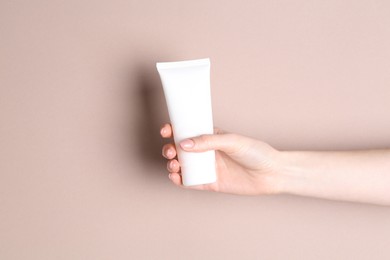 Photo of Woman with tube of cream on beige background, closeup