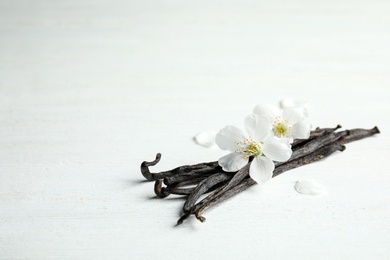 Photo of Aromatic vanilla sticks and flowers on wooden background, space for text