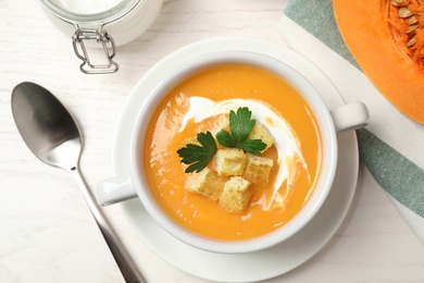 Photo of Delicious pumpkin soup in bowl served on white wooden table, flat lay