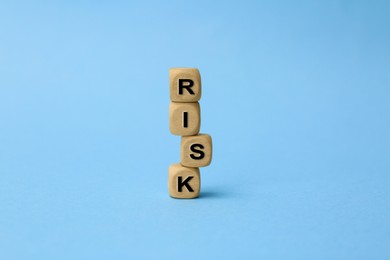 Photo of Stack of wooden cubes with word Risk on light blue background