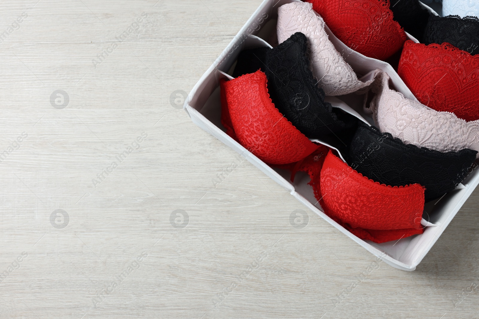 Photo of Organizer with folded women's underwear on light wooden table, top view. Space for text