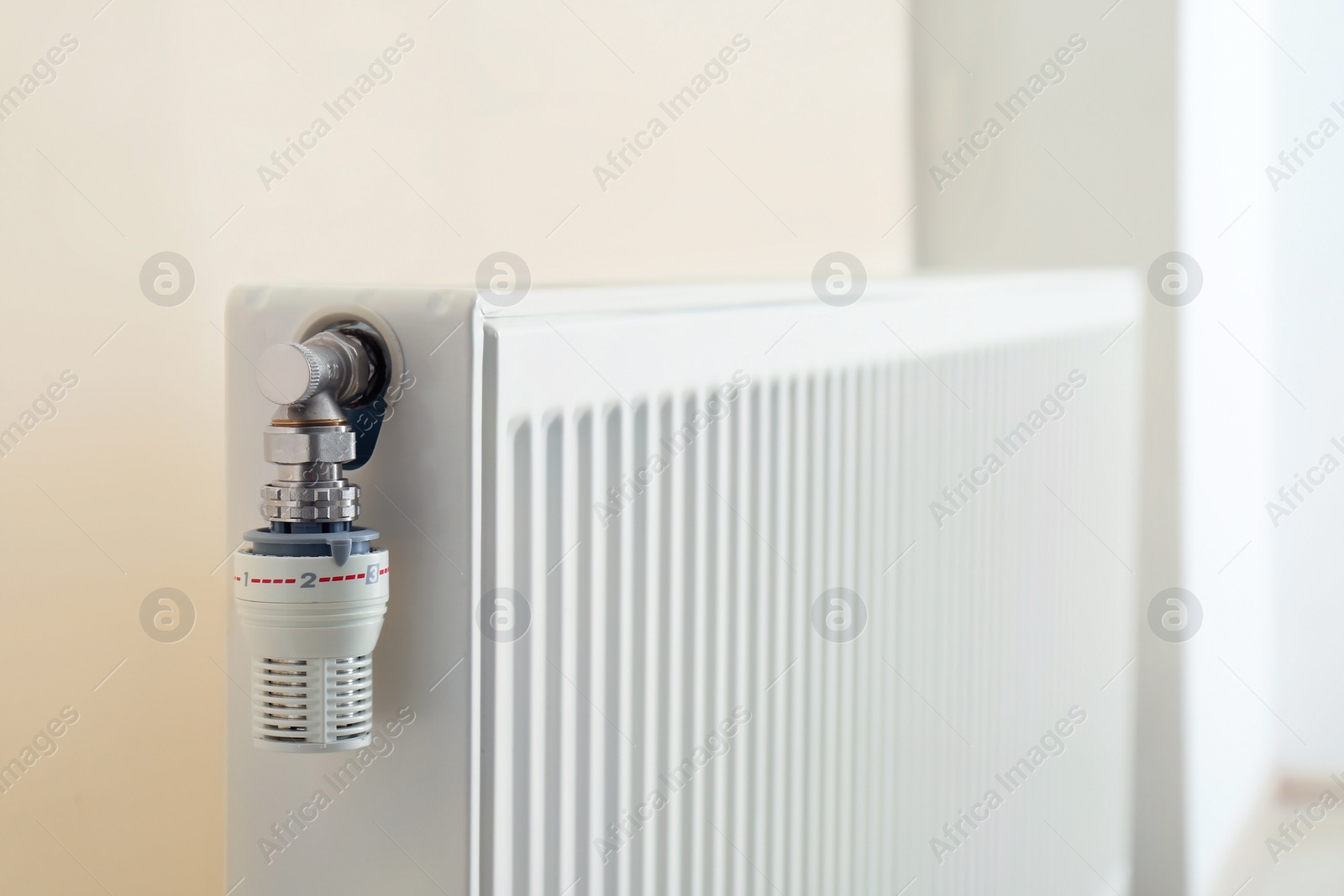 Photo of Heating radiator with thermostat near light wall indoors