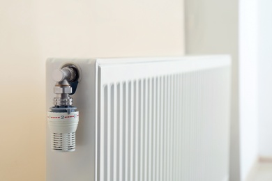 Heating radiator with thermostat near light wall indoors