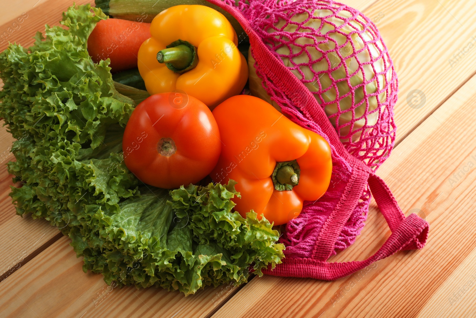 Photo of Net bag with vegetables on wooden table, closeup